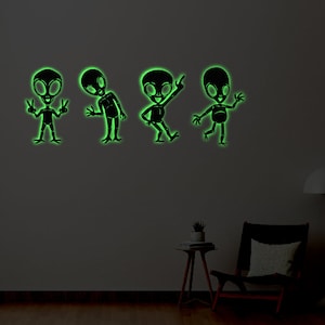 May include: Four glow-in-the-dark alien wall decals in various poses. The aliens are black silhouettes against a dark green wall.