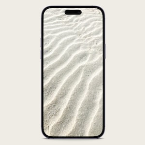 May include: A close-up of a smartphone displaying a photo of white sand with wave patterns.