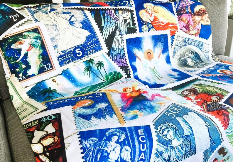 May include: A throw blanket with a design of vintage postage stamps depicting angels and religious figures. The stamps are in shades of blue, white, red, and green. The blanket is displayed on a grey surface.