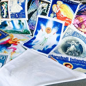 May include: A white blanket printed with a collection of vintage postage stamps. The stamps depict angels in various poses and colors, including blue, yellow, and red. Text includes "Barbados" and "Marshall Islands".