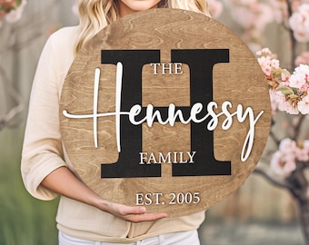 May include: A round wooden sign with the text "The Hennessy Family Est. 2005" in white lettering on a black background. The letter "H" is large and three-dimensional.