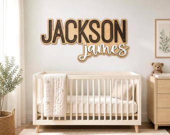 May include: A wooden sign with the name "JACKSON JAMES" in a nursery setting. The word "JACKSON" is in bold, black letters, and "James" is in a cursive font. A white crib, dresser, and rug complete the room.
