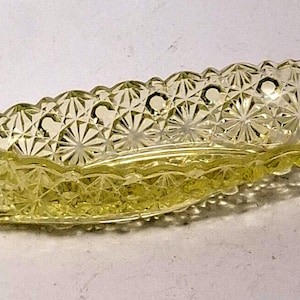 May include: A vintage, oblong-shaped, yellow glass dish. The dish has a detailed, starburst and diamond pattern. The edges are scalloped. This decorative piece is likely used for serving or display.