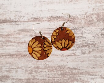 May include: A pair of brown leather earrings with a floral design. The earrings are round and have a silver hook.