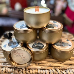 May include: A stack of gold candle jars with various inspirational quotes and designs. The top candle jar has a wooden wick with the word "HOPE" written on it.
