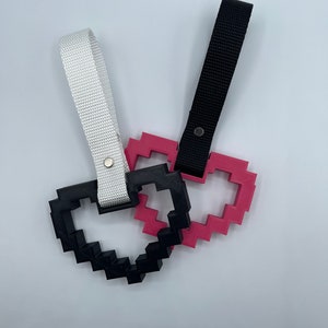 Op de afbeelding: Twee hartvormige sleutelhangers, een zwart en een roze, met witte en zwarte banden.