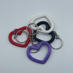 May include: A set of five heart-shaped keychains in red, white, black, and purple. The keychains are connected by a silver chain.