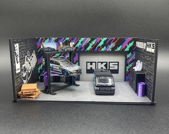 May include: A miniature garage diorama with a black and white car on a lift, a black van, and a brick wall with the text "Powered by HKS".