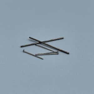 以下が含まれることがあります： 白い表面に、先が尖ったものと丸いものがある、銀色の金属製のピンが6本散らばっている。