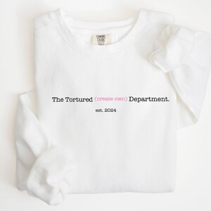 Op de afbeelding: Witte trui met zwarte tekst die "The Tortured (create own) Department. est. 2024" luidt.