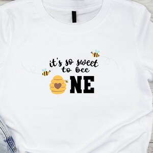 May include: White t-shirt with the text "it's so sweet to bee one" in black. The text is surrounded by small bee illustrations.
