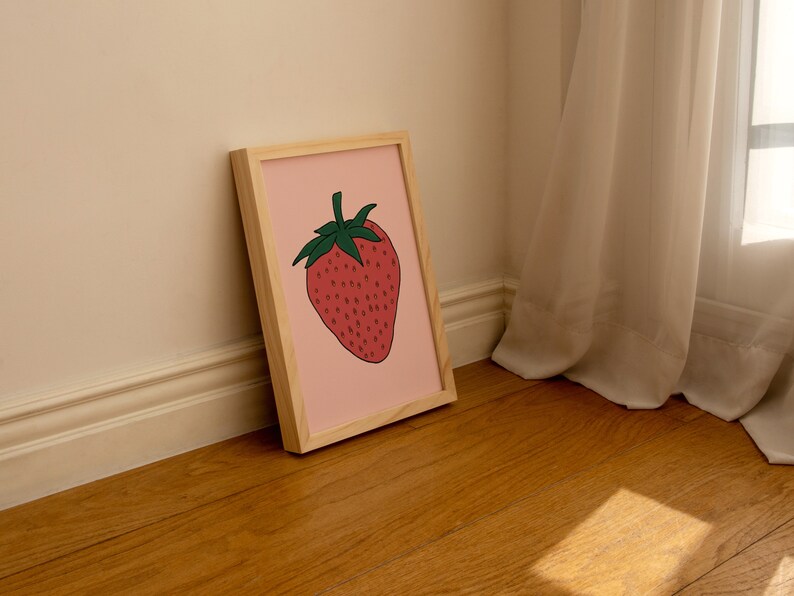 May include: A framed illustration of a red strawberry with green leaves on a pink background. The frame is made of light wood.