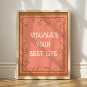 May include: A framed print with a peach background and gold ornate border. The text "Visualize Your Best Life" is written in a retro font.