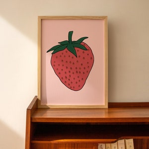 May include: A framed print of a red strawberry with green leaves on a pink background.