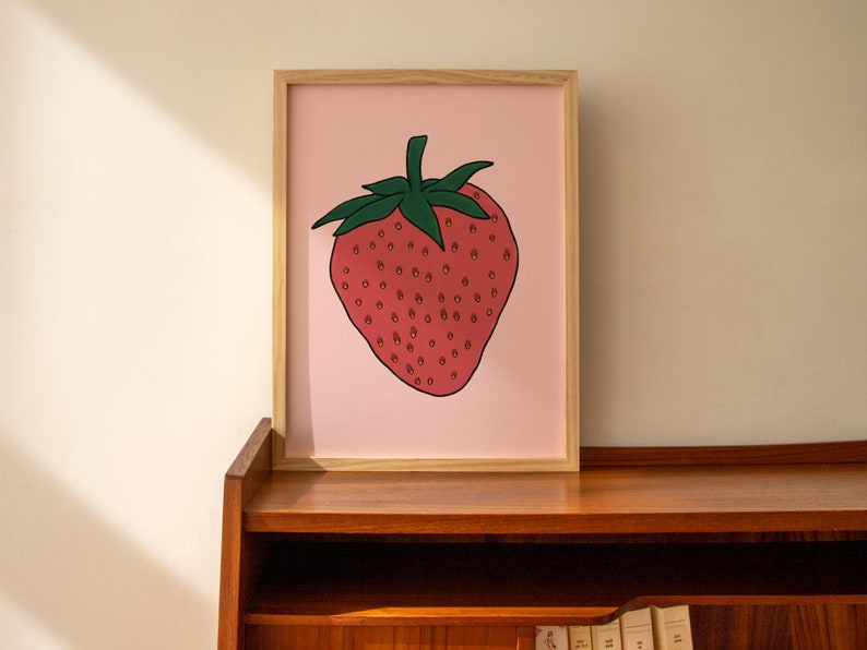 May include: A framed print of a red strawberry with green leaves on a pink background.