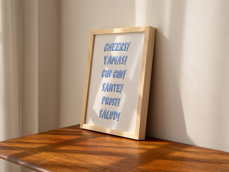 May include: A framed print with the words "CHEERS! YAMAS! CIN CIN! SANTE! PROST! SALUD!" in blue text on a white background.