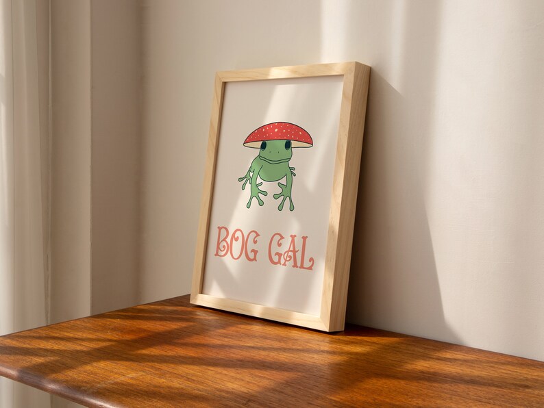 May include: A framed print with a cartoon frog wearing a red and white mushroom hat. The text "BOG GAL" is printed below the frog.