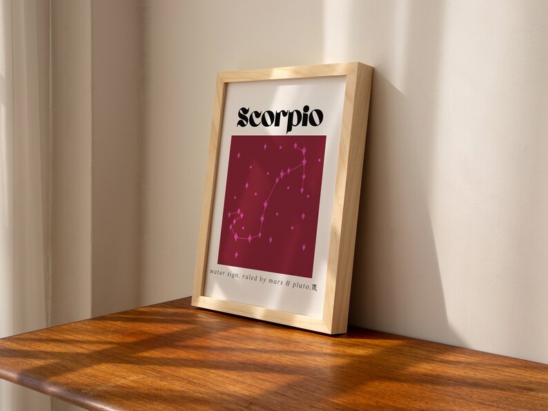 May include: A framed print with a burgundy background and a pink constellation of the Scorpio zodiac sign. The text "Scorpio" is in black bold letters at the top of the print. The text "water sign, ruled by mars & pluto" is at the bottom of the print.