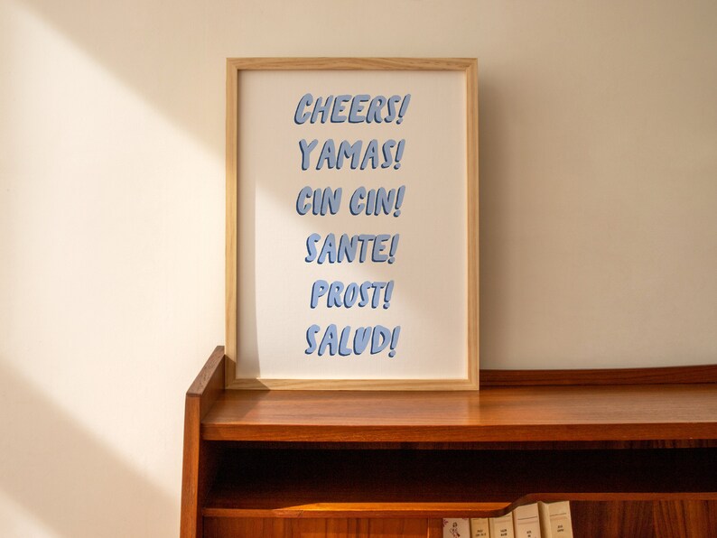 May include: A framed print with the words "CHEERS! YAMAS! CIN CIN! SANTE! PROST! SALUD!" in blue text on a white background.