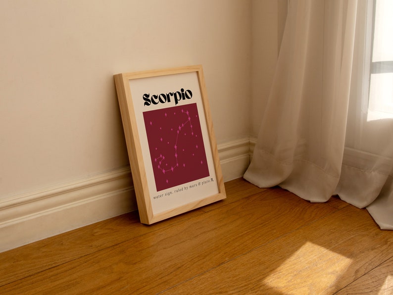 May include: A framed print with a burgundy background and a pink constellation of the Scorpio zodiac sign. The text "Scorpio" is in black bold letters at the top of the print. The text "water sign, ruled by mars & pluto" is at the bottom of the print.