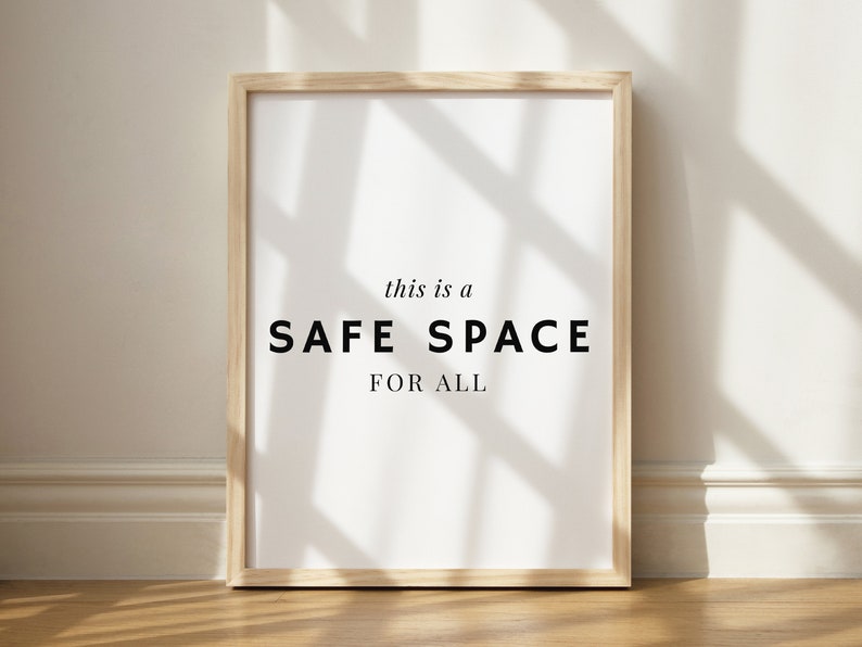 May include: A framed print with the text "this is a SAFE SPACE FOR ALL" on a white background. The frame is light wood and the print is hanging on a white wall.