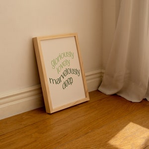May include: A wooden framed print with the words "gloriously lovely marvelously deep" written in green on a cream background.