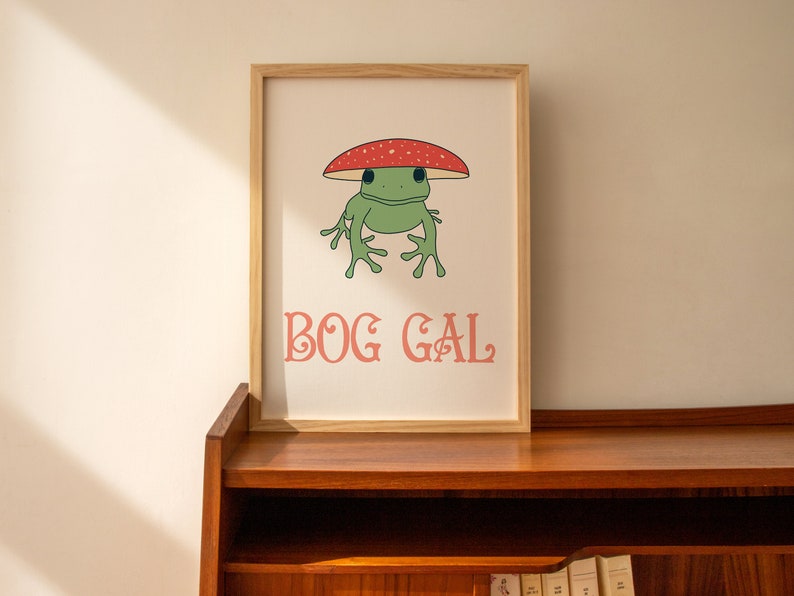 May include: A framed print with a green frog wearing a red and white mushroom hat. The text "BOG GAL" is printed in pink below the frog.