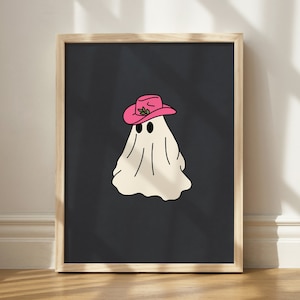 May include: A framed print of a white ghost wearing a pink cowboy hat with green leaves on a black background.