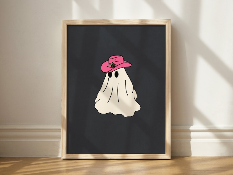 May include: A framed print of a white ghost wearing a pink cowboy hat with green leaves on a black background.