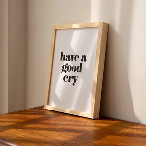 K&ouml;nnte beinhalten: Ein gerahmter Druck mit dem Text "have a good cry" in schwarzen Fettdruck auf wei&szlig;em Hintergrund. Der Rahmen ist aus hellem Holz.