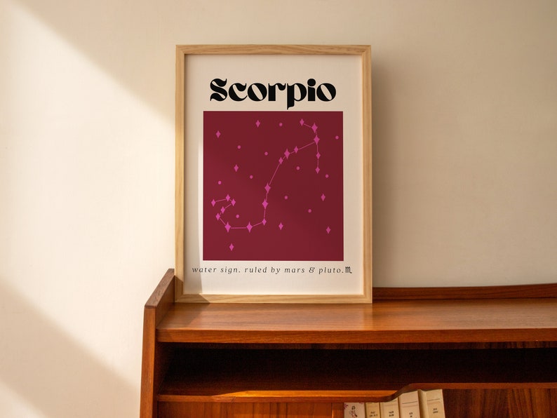 May include: A framed print with a burgundy background and a pink constellation of the zodiac sign Scorpio. The text "Scorpio" is in black bold font and the text "water sign. ruled by mars & pluto." is in smaller black font.