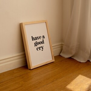 K&ouml;nnte beinhalten: Ein gerahmter Druck mit dem Text "have a good cry" in schwarzen Fettdruck auf wei&szlig;em Hintergrund. Der Rahmen ist aus hellem Holz und steht auf einem Holzboden.