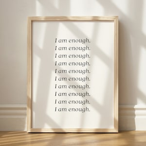 May include: A framed print with the text "I am enough." repeated ten times in a simple black font on a white background.