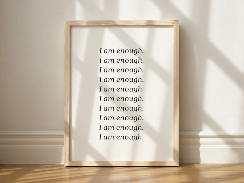 May include: A framed print with the text "I am enough." repeated ten times in a simple black font on a white background.