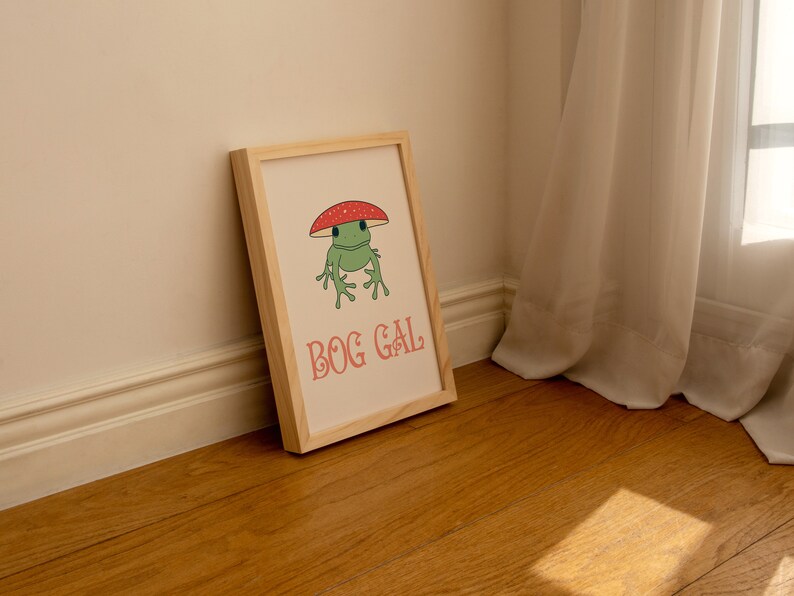 May include: A framed print with a cartoon frog wearing a red and white mushroom on its head. The text "BOG GAL" is printed in pink below the frog.