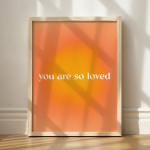 May include: A framed print with a gradient background of orange and yellow. The text "you are so loved" is printed in white on the print.