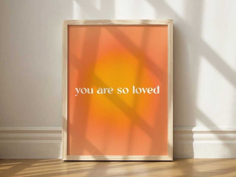 May include: A framed print with a gradient background of orange and yellow. The text "you are so loved" is printed in white on the print.