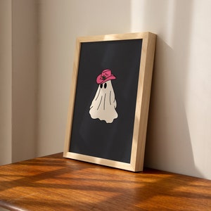 May include: A framed print of a white ghost wearing a pink cowboy hat on a black background.