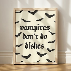 May include: A framed print with a light yellow background and black bats. The print says "vampires don't do dishes" in black gothic font.