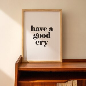K&ouml;nnte beinhalten: Ein gerahmter Druck mit dem Text "have a good cry" in schwarzen Fettdruck auf wei&szlig;em Hintergrund. Der Rahmen ist aus hellem Holz und der Druck steht auf einem Holzregal.