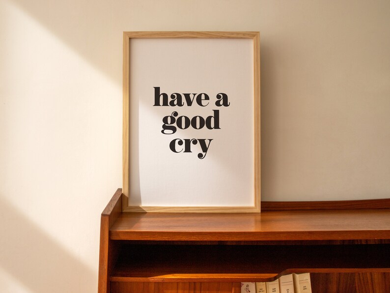 K&ouml;nnte beinhalten: Ein gerahmter Druck mit dem Text "have a good cry" in schwarzen Fettdruck auf wei&szlig;em Hintergrund. Der Rahmen ist aus hellem Holz und der Druck steht auf einem Holzregal.