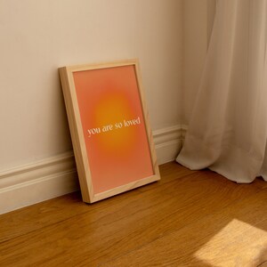 May include: A framed print with a peach and orange gradient background and the text "you are so loved" in white.