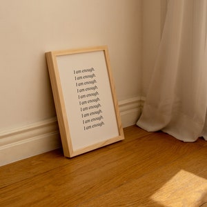 May include: A wooden framed print with the text "I am enough." repeated 10 times in black font on a white background.