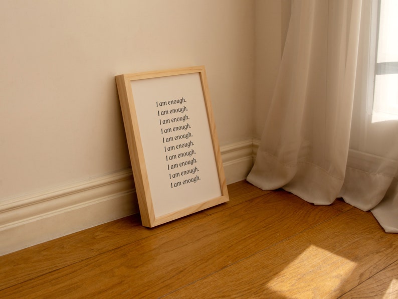 May include: A wooden framed print with the text "I am enough." repeated 10 times in black font on a white background.