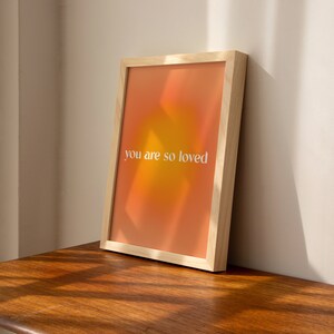 May include: A framed print with a gradient background of orange and yellow. The text "you are so loved" is printed in white on the print.