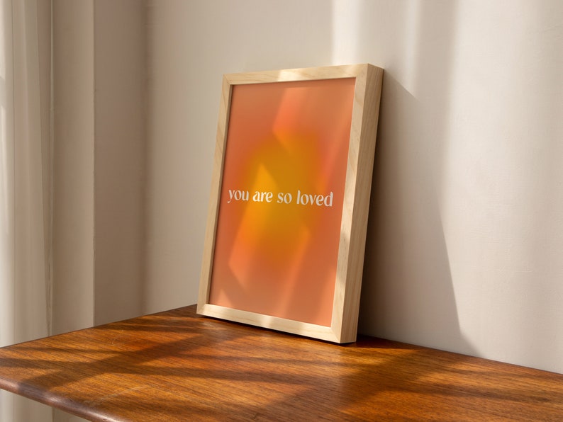 May include: A framed print with a gradient background of orange and yellow. The text "you are so loved" is printed in white on the print.