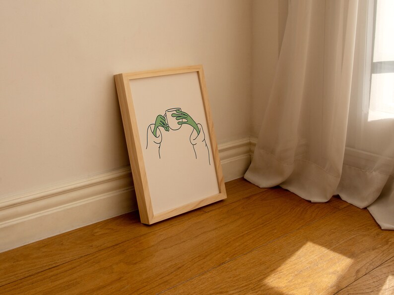 May include: A framed illustration of a person holding a cup with their hands. The illustration is in black and green line art on a cream background.