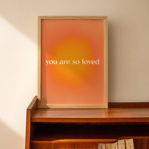 May include: A framed print with a gradient background of orange and yellow. The text "you are so loved" is printed in white on the print.