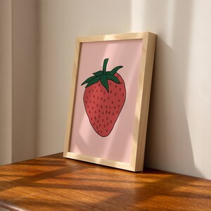 May include: A framed print of a red strawberry with green leaves on a pink background.