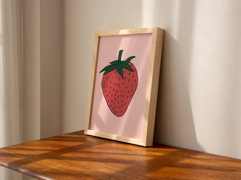 May include: A framed print of a red strawberry with green leaves on a pink background.
